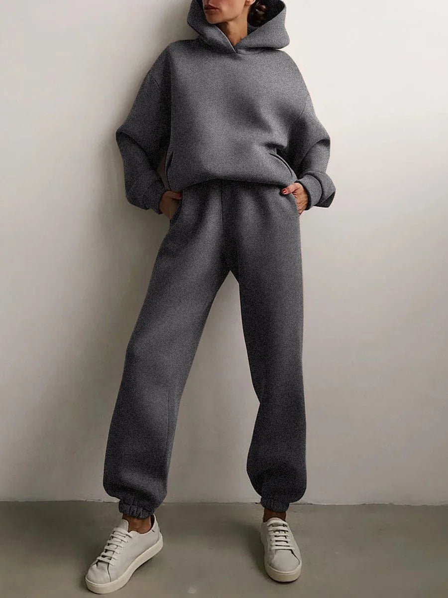 Cozy grey oversized hoodie with matching high-waisted joggers, styled with white sneakers and hands in pockets.