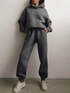Cozy grey oversized hoodie with matching high-waisted joggers, styled with white sneakers and hands in pockets.