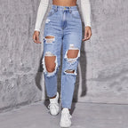 High-waisted distressed straight-leg denim jeans in light blue, featuring large rips and raw edges, paired with white sneakers.