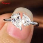 Double pear-cut Moissanite statement ring in 925 sterling silver, set asymmetrically, held between fingers, showcasing brilliance.