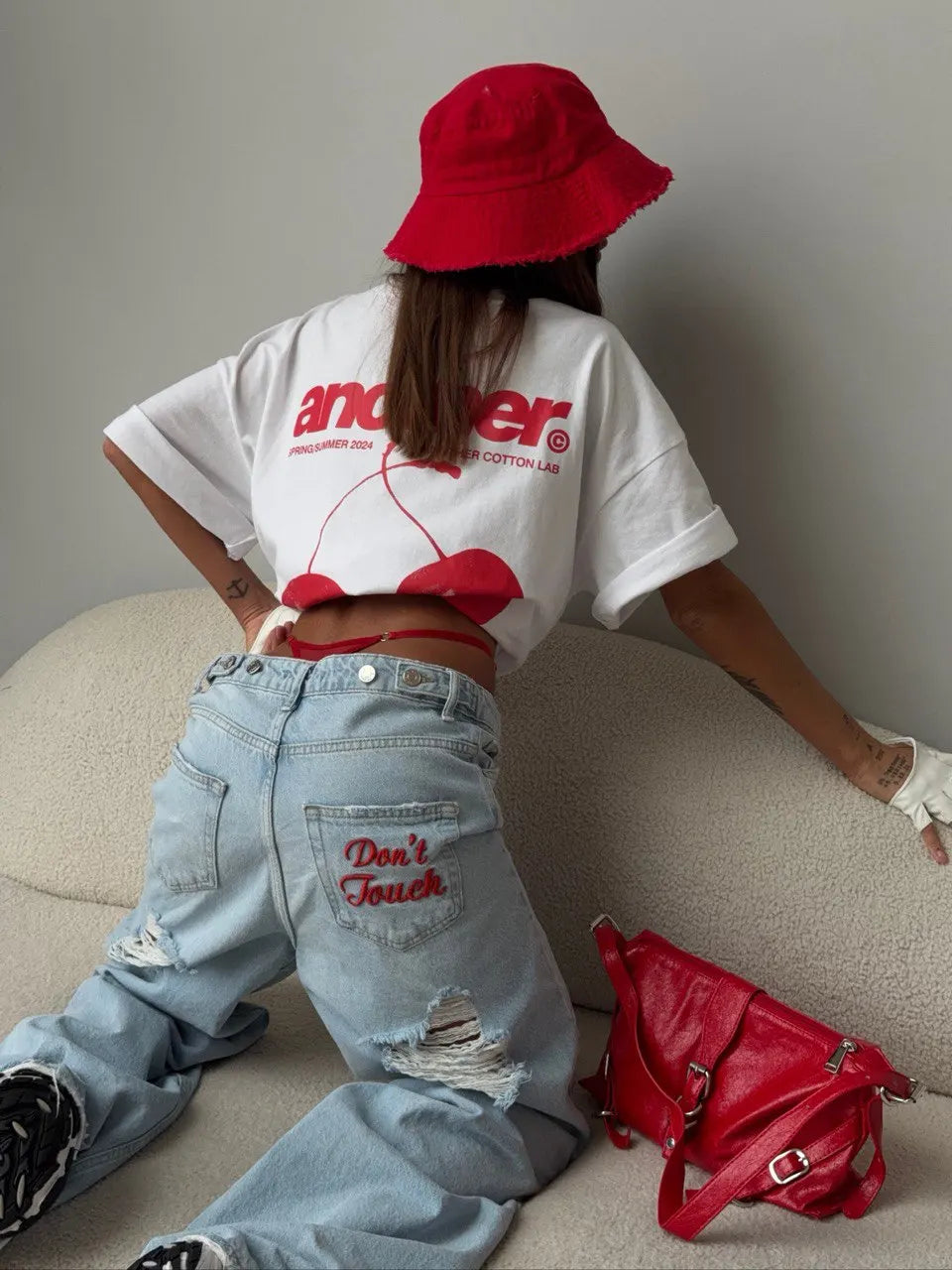 Distressed light blue baggy denim jeans with red "Don't Touch" embroidery, styled with an oversized white tee and red bucket hat.