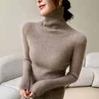 Slim-fit turtleneck in soft beige cashmere, featuring ribbed texture and high collar, worn with hands positioned at the waist.