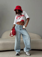 Baggy light blue distressed denim jeans with embroidered details, worn with a cropped white t-shirt and red accessories.