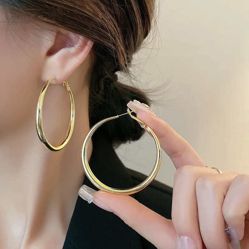 Chunky gold minimalist hoop earrings held by a model, showcasing their high-gloss finish and hollow design.