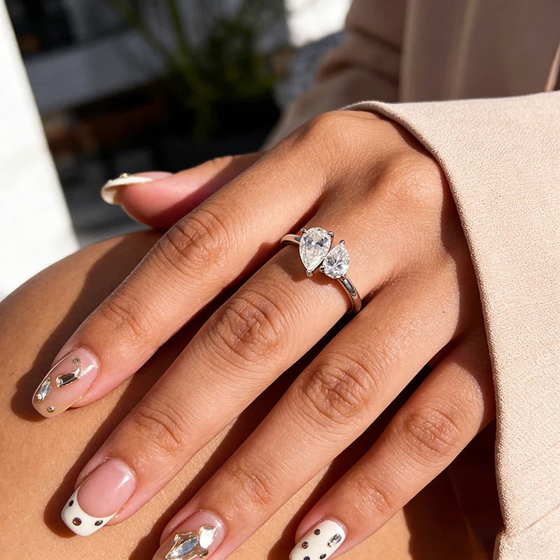 Sterling silver ring featuring two pear-cut Moissanite stones in a modern asymmetric design, worn on a hand with stylish nails.