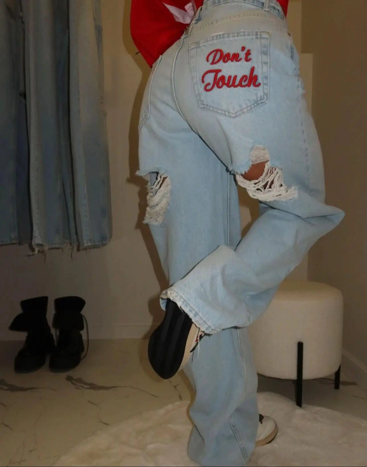 Light blue baggy distressed denim jeans with red "Don't Touch" embroidery, oversized fit, showcasing knee rips.