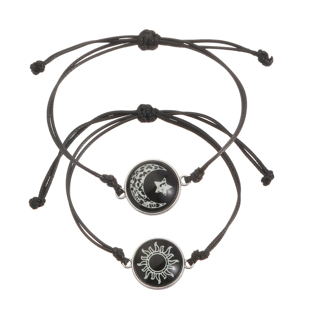 Two black rope bracelets featuring round charms: one with a moon and star design, the other with a sun emblem.