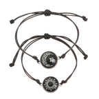 Two black rope bracelets featuring round charms: one with a moon and star design, the other with a sun emblem.