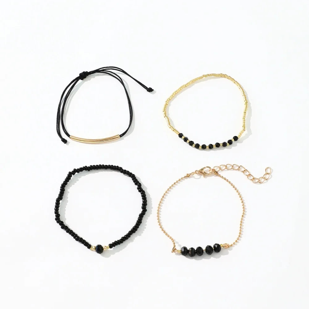 Four stackable bracelets in a mix of black onyx glass stones and metallic gold-tone beads.