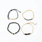 Four stackable bracelets in a mix of black onyx glass stones and metallic gold-tone beads.