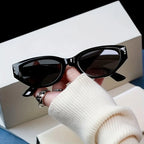Chunky cat-eye sunglasses with a high-gloss black finish, held in a hand wearing a cream sweater.