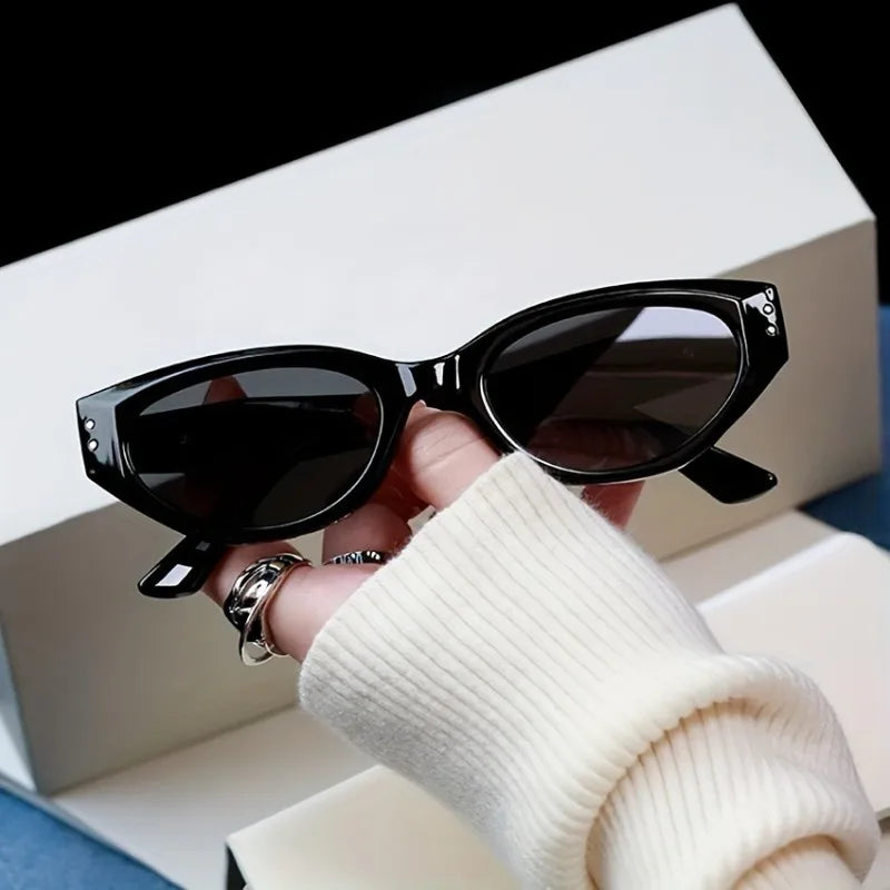 Chunky cat-eye sunglasses with a high-gloss black finish, held in a hand wearing a cream sweater.