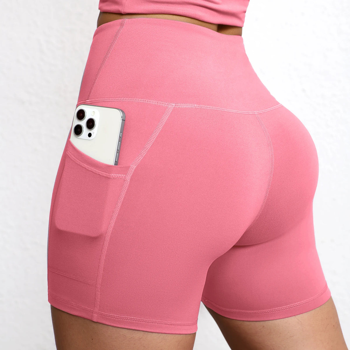 High-waisted pink yoga shorts with integrated side pocket holding a smartphone, featuring a seamless design and sculpting fit.