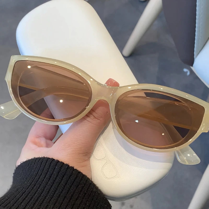 Vintage cat-eye sunglasses with a creamy translucent frame and brown tinted lenses, held in a hand against a light background.