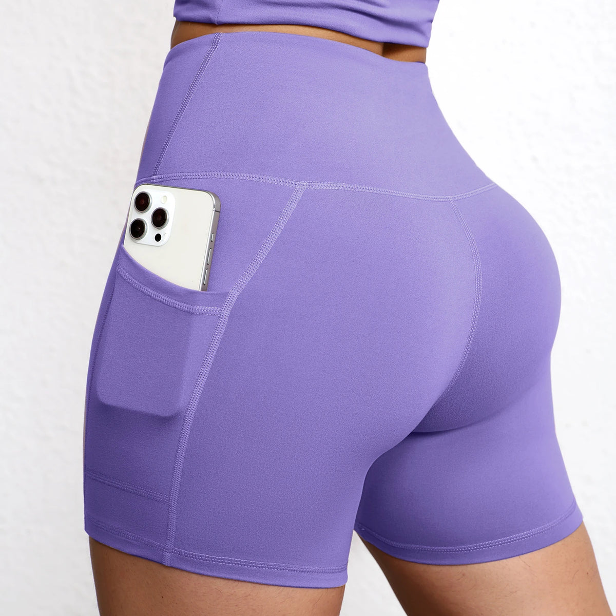 High-waisted seamless yoga shorts in lavender with a side pocket holding a smartphone, featuring a sculpting fit.