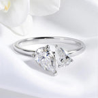 Statement ring with two pear-cut Moissanite stones in a silver setting, resting on soft white fabric.