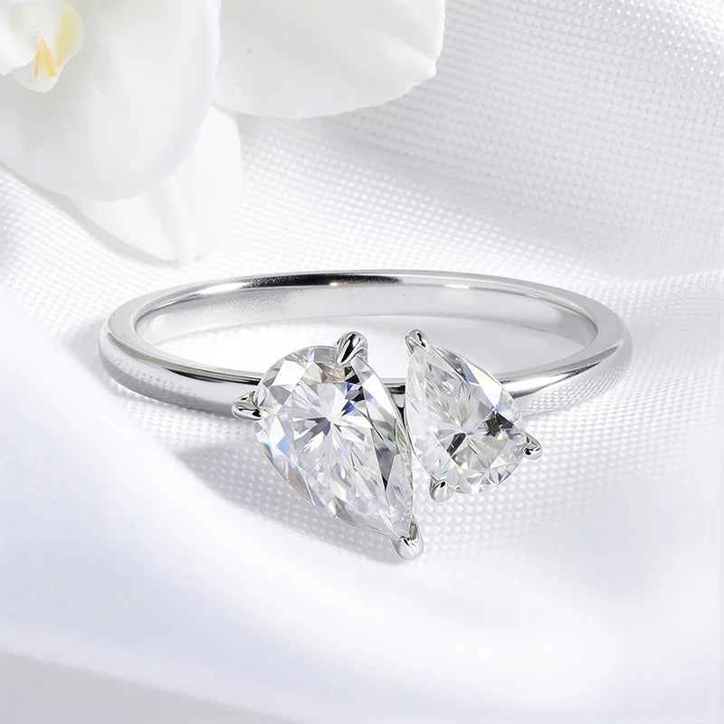 Statement ring with two pear-cut Moissanite stones in a silver setting, resting on soft white fabric.