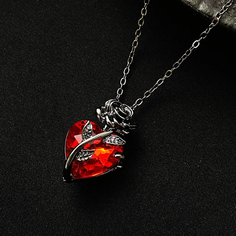 Crimson anatomical heart pendant wrapped in dark floral metalwork on a delicate chain, showcasing gothic style.