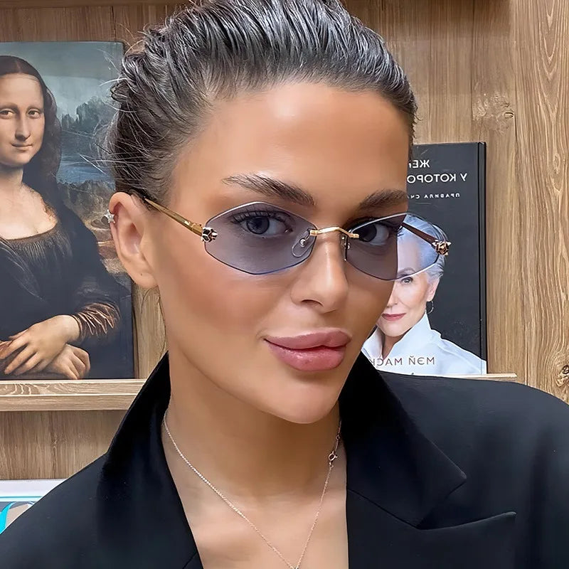 Rimless rhombus sunglasses with grey lenses and gold metal temples worn by a woman in a black blazer.