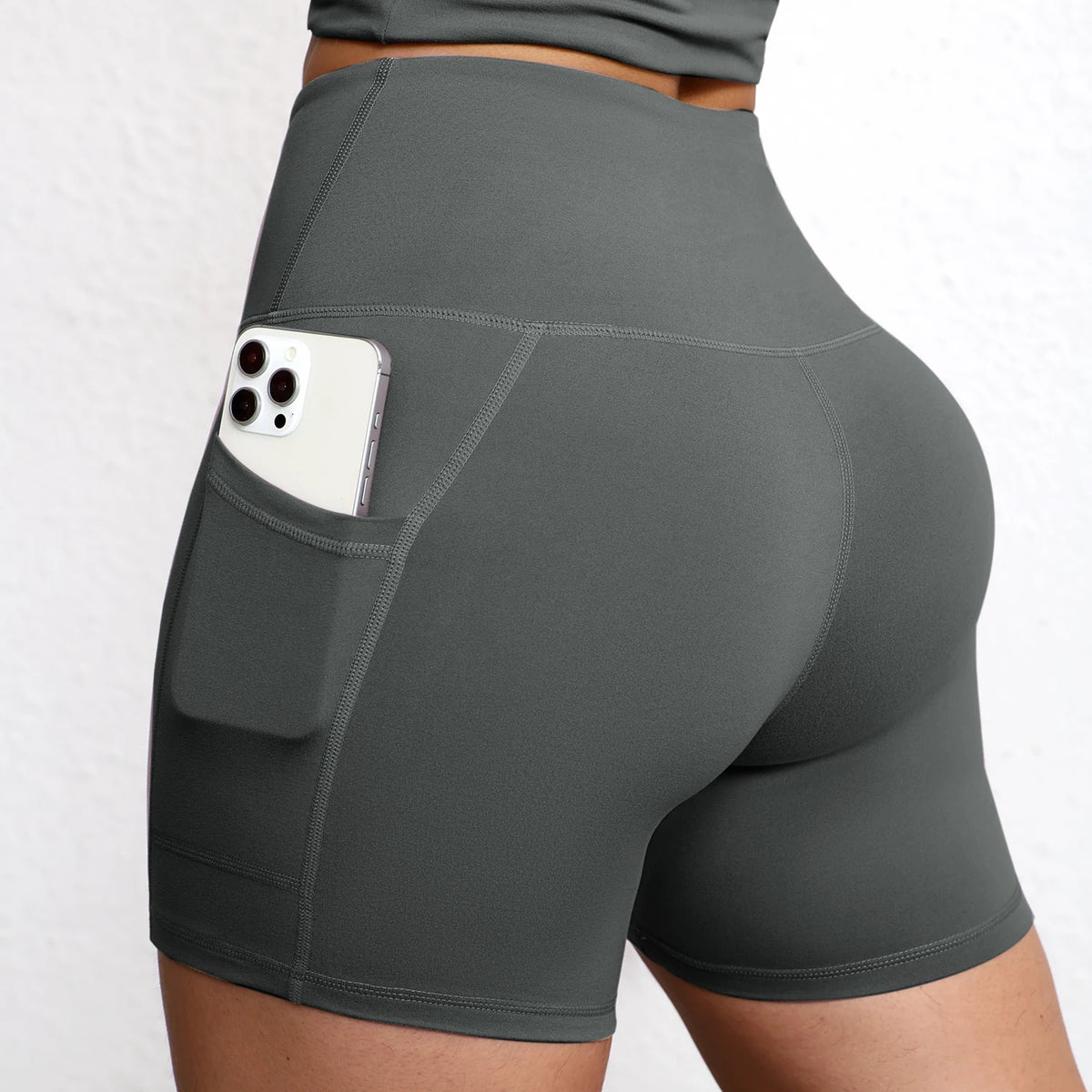 High-waisted seamless yoga shorts in dark gray with side pockets and a smooth fit, showcasing a smartphone tucked in the pocket.