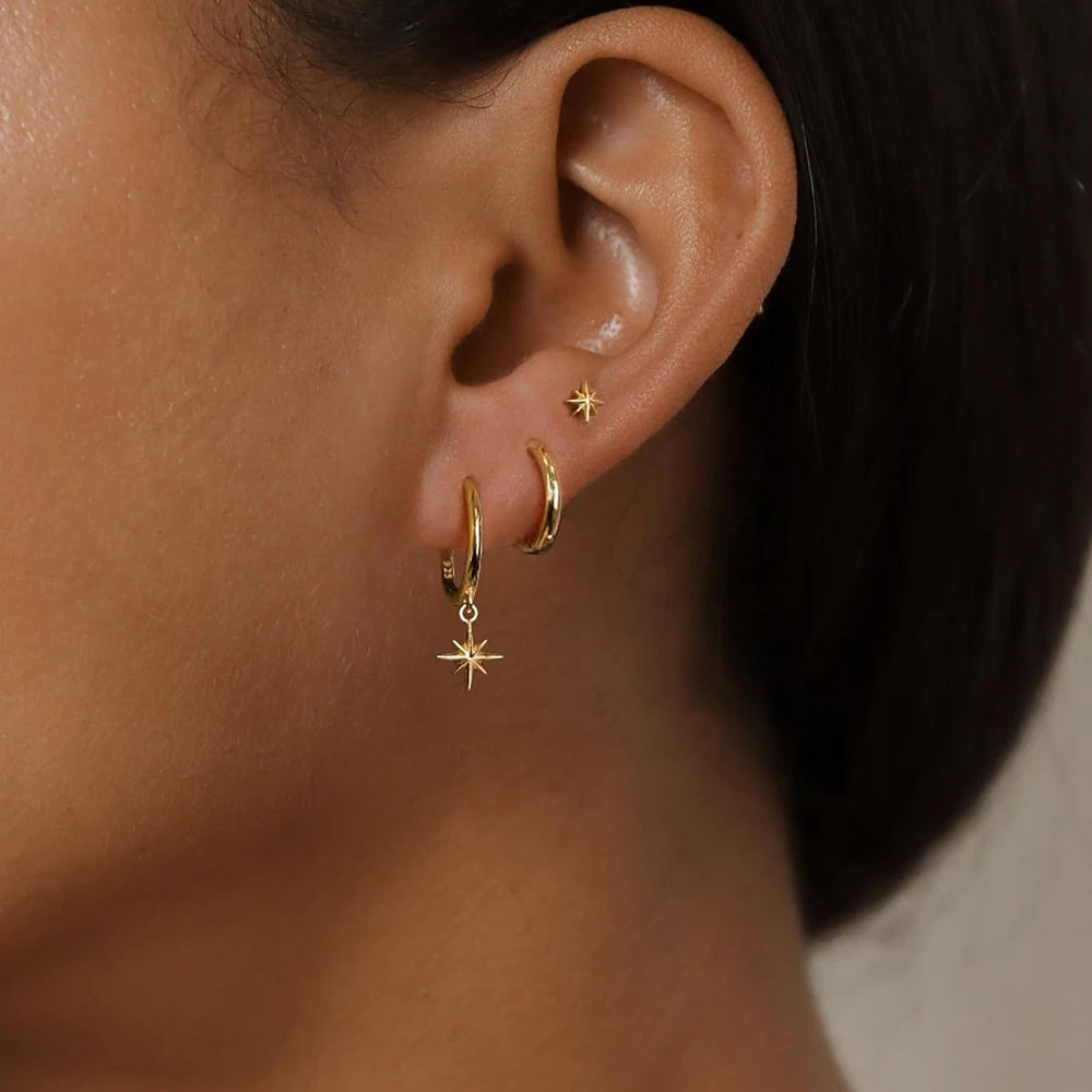 Gold-toned waterproof stainless steel earring set featuring geometric shapes: a star, hoop, and stud, worn on one ear.