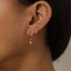 Gold-toned waterproof stainless steel earring set featuring geometric shapes: a star, hoop, and stud, worn on one ear.