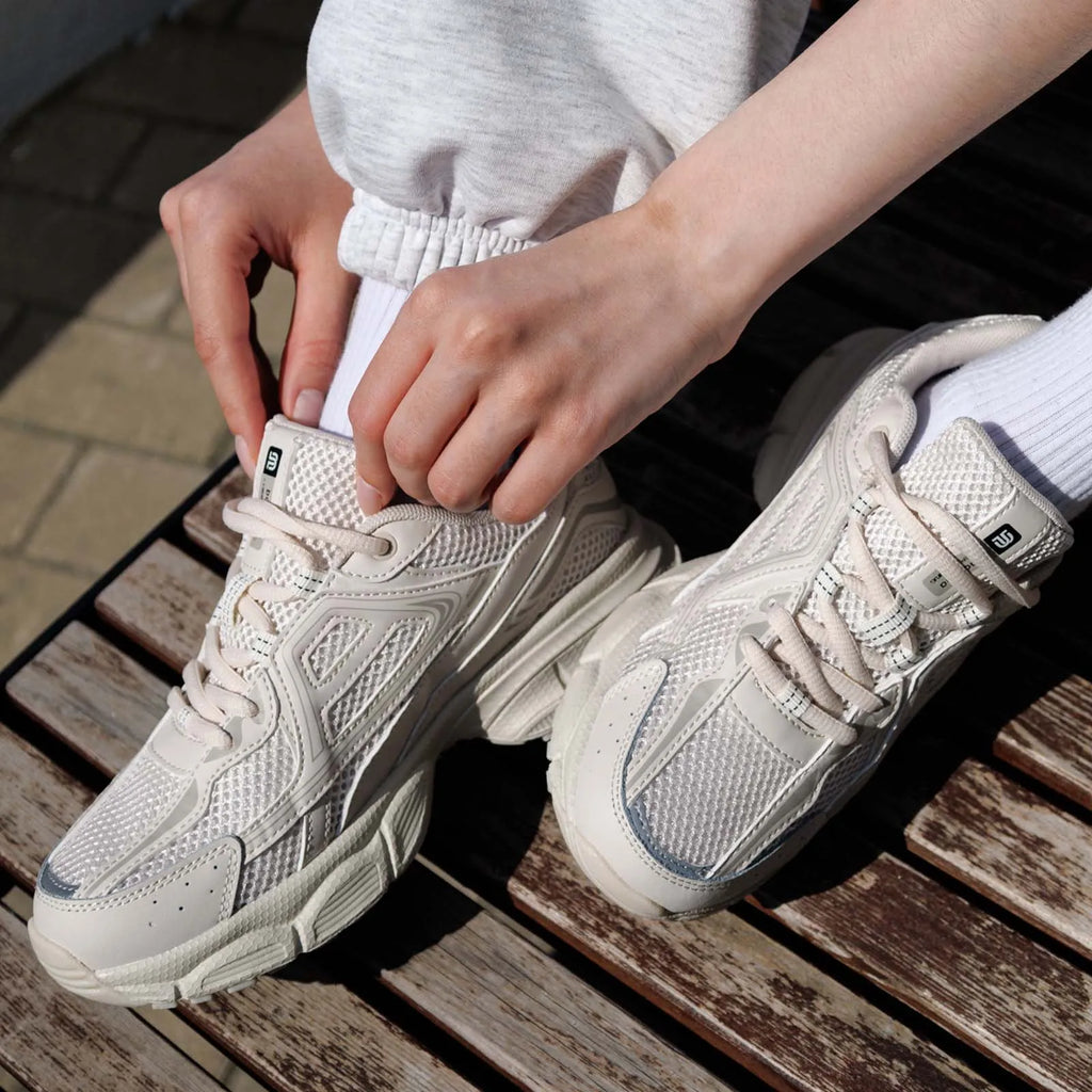 Chunky cream sneakers with breathable mesh panels, showcased on a seated person adjusting the laces.