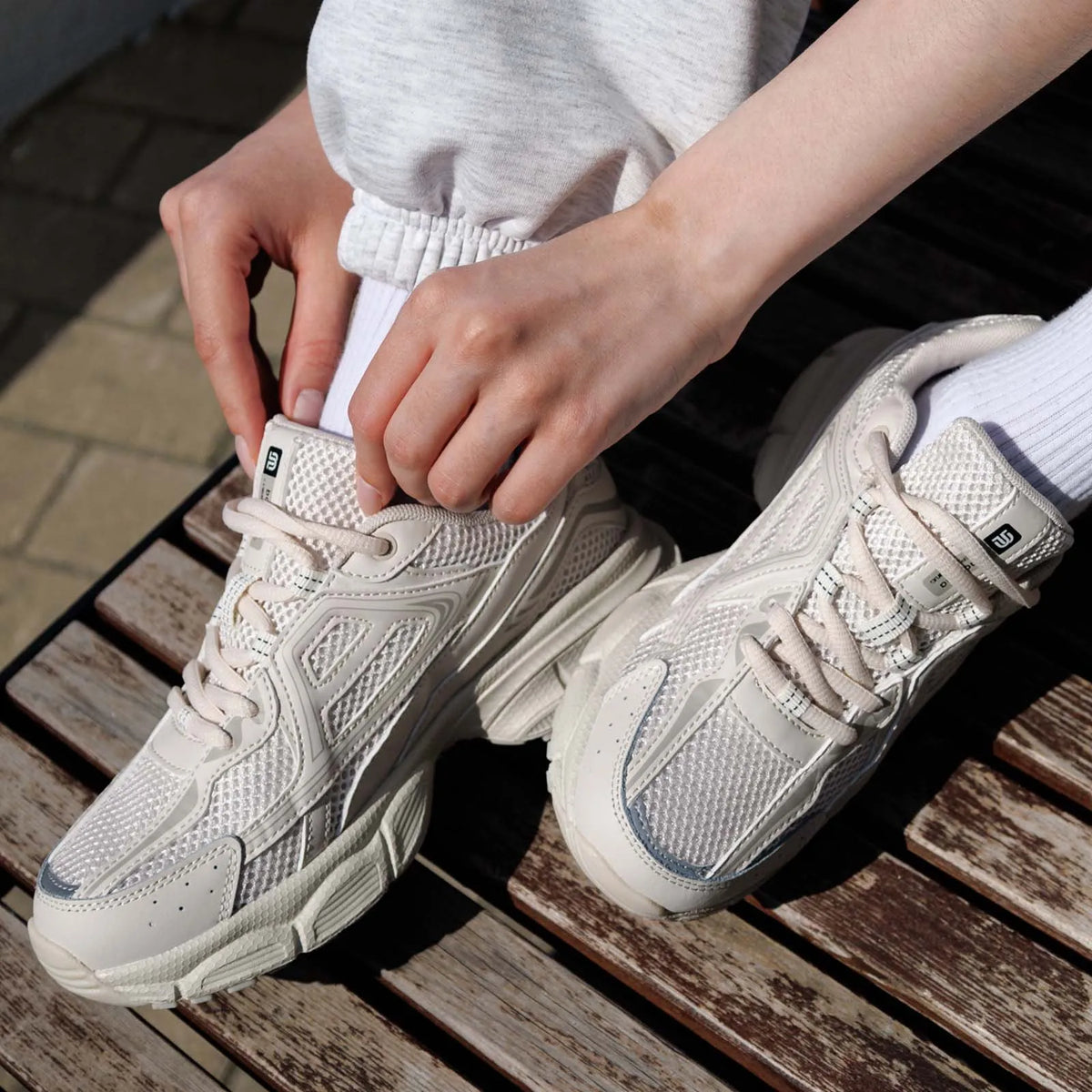 Chunky cream sneakers with breathable mesh panels, showcased on a seated person adjusting the laces.