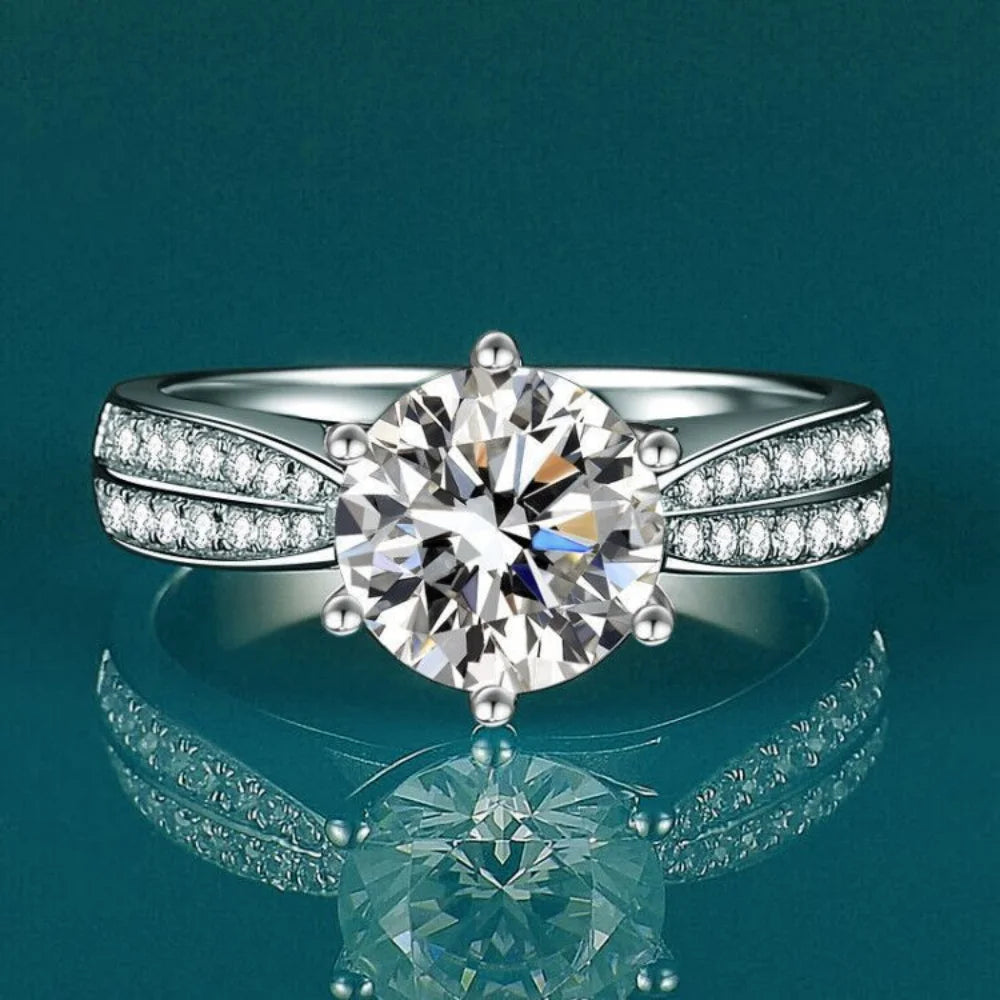 Round-cut Moissanite stone set in a high-polish 925 sterling silver band, featuring smaller stones on the band for added sparkle.