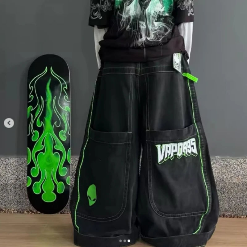 Baggy distressed denim jeans featuring green embroidered lettering, oversized wide-leg cut, and alien graphic detail.