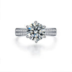 Round-cut Moissanite center stone surrounded by smaller stones, set in a polished 925 sterling silver band.