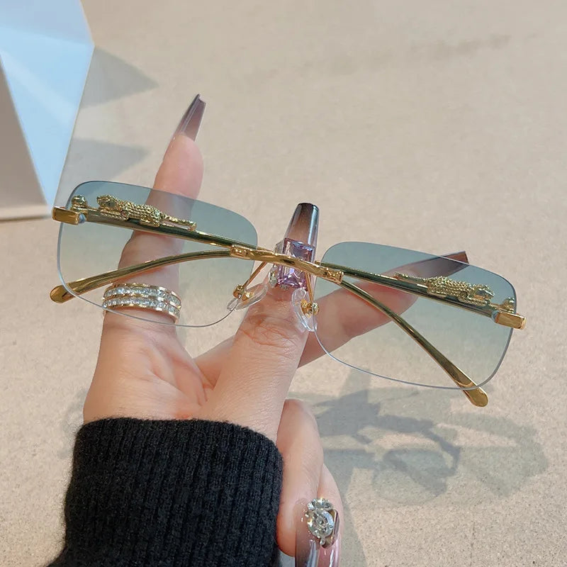 Rimless Y2K rectangle sunglasses with gradient lenses, metallic accents, and gold detailing, held by a hand with stylish rings.