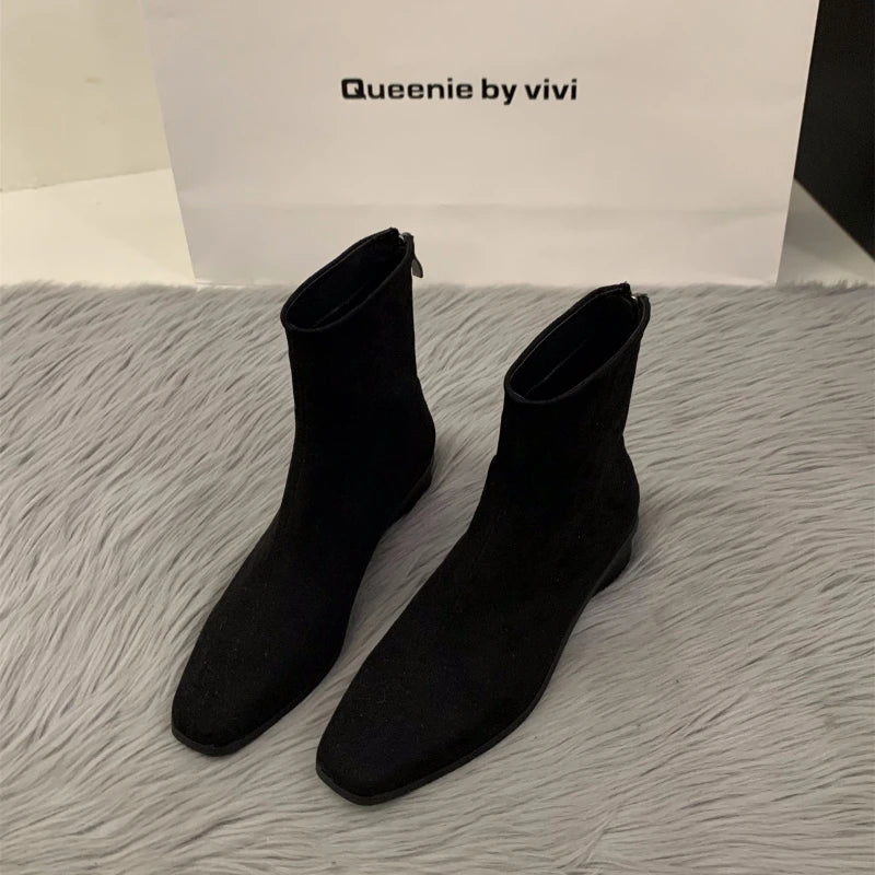 Black suede ankle boots with a sleek design, featuring a back zipper and a low stacked heel.
