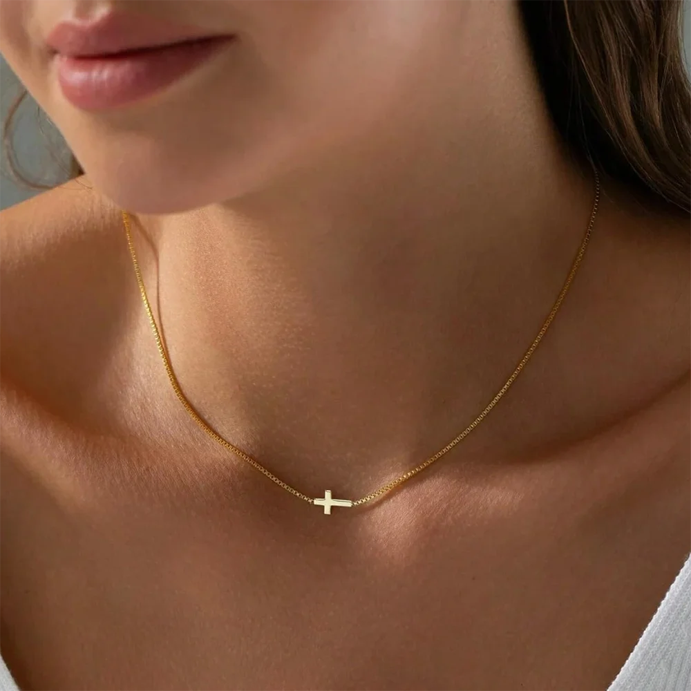 Gold minimalist cross necklace worn on the collarbone, featuring a delicate chain and a high-polish mini cross pendant.