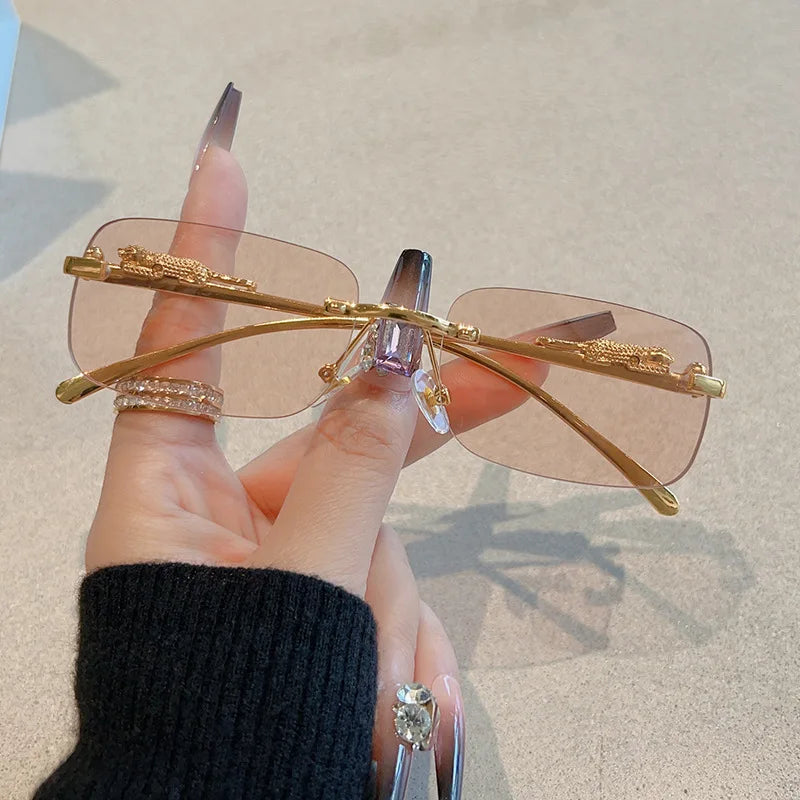Rimless Y2K rectangle sunglasses with gradient lenses and metallic gold accents, held by a hand with long nails.