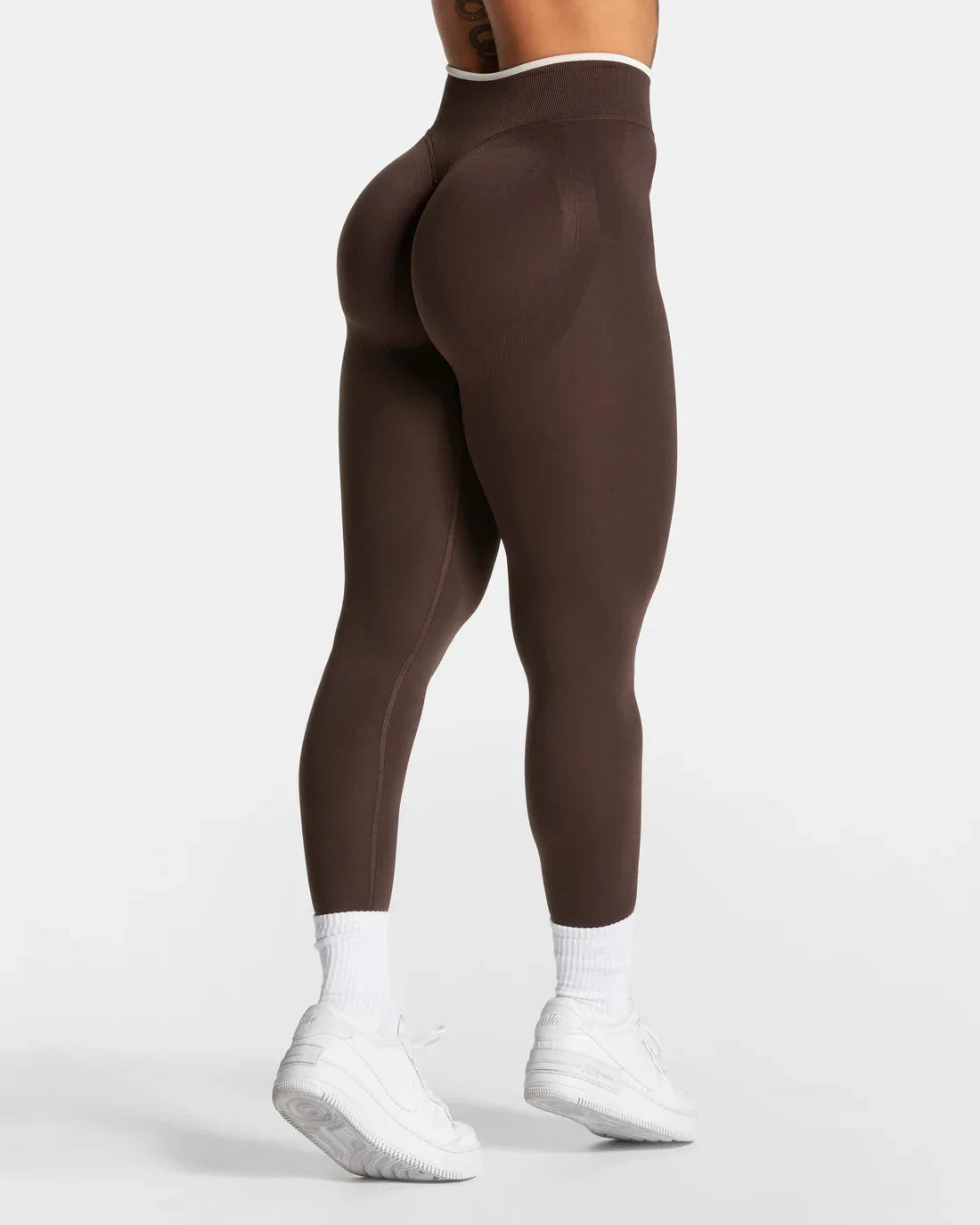 High-waisted brown seamless leggings with contrasting white waistband, fitted to a model wearing white sneakers.