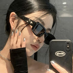 Black wrap-around sunglasses with a sleek, aerodynamic frame, worn by a model with long dark hair and metallic nails.