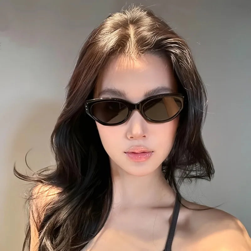 Chunky cat-eye sunglasses with a high-gloss dark frame, worn by a model with long, wavy hair, featuring dark lenses.