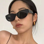 Cat-eye sunglasses with a sleek black frame, worn by a model with minimal makeup and golden hoop earrings.