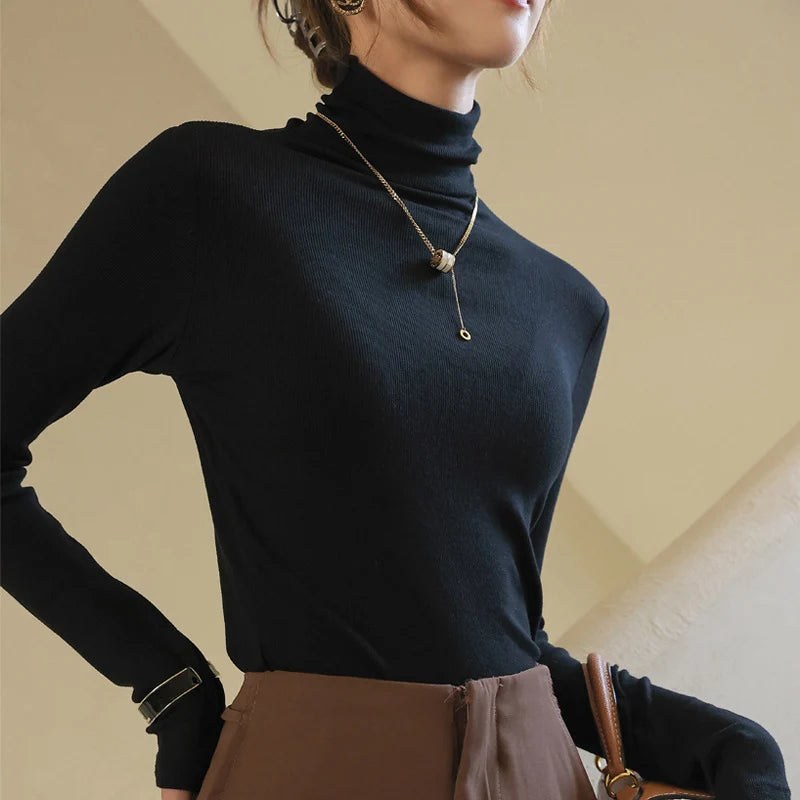 Black slim-fit mock-neck pullover with high-density ribbed texture, paired with brown pants and layered gold necklace.