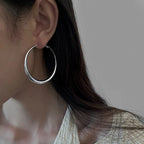 Hollow, chunky minimalist hoop earrings in shiny silver worn on the model's ear, highlighting a sleek design.