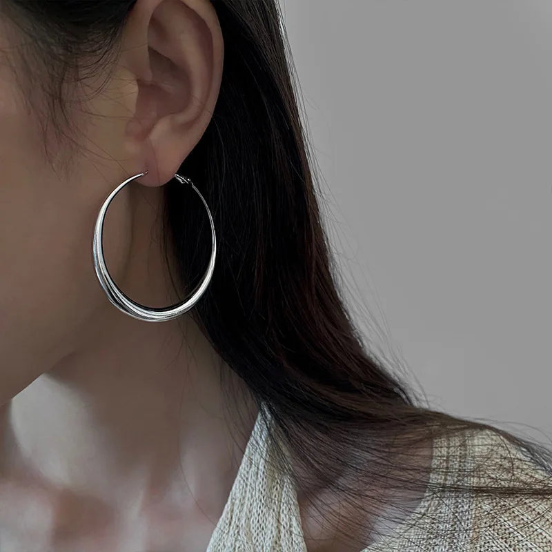 Hollow, chunky minimalist hoop earrings in shiny silver worn on the model's ear, highlighting a sleek design.