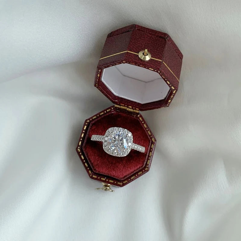 Round-cut Moissanite ring in a red octagonal box, featuring a halo of micro-pave crystals on a silver band.