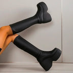 Ultra-chunky black platform boots with a curved block heel and sleek eco-leather finish, styled for a dramatic look.