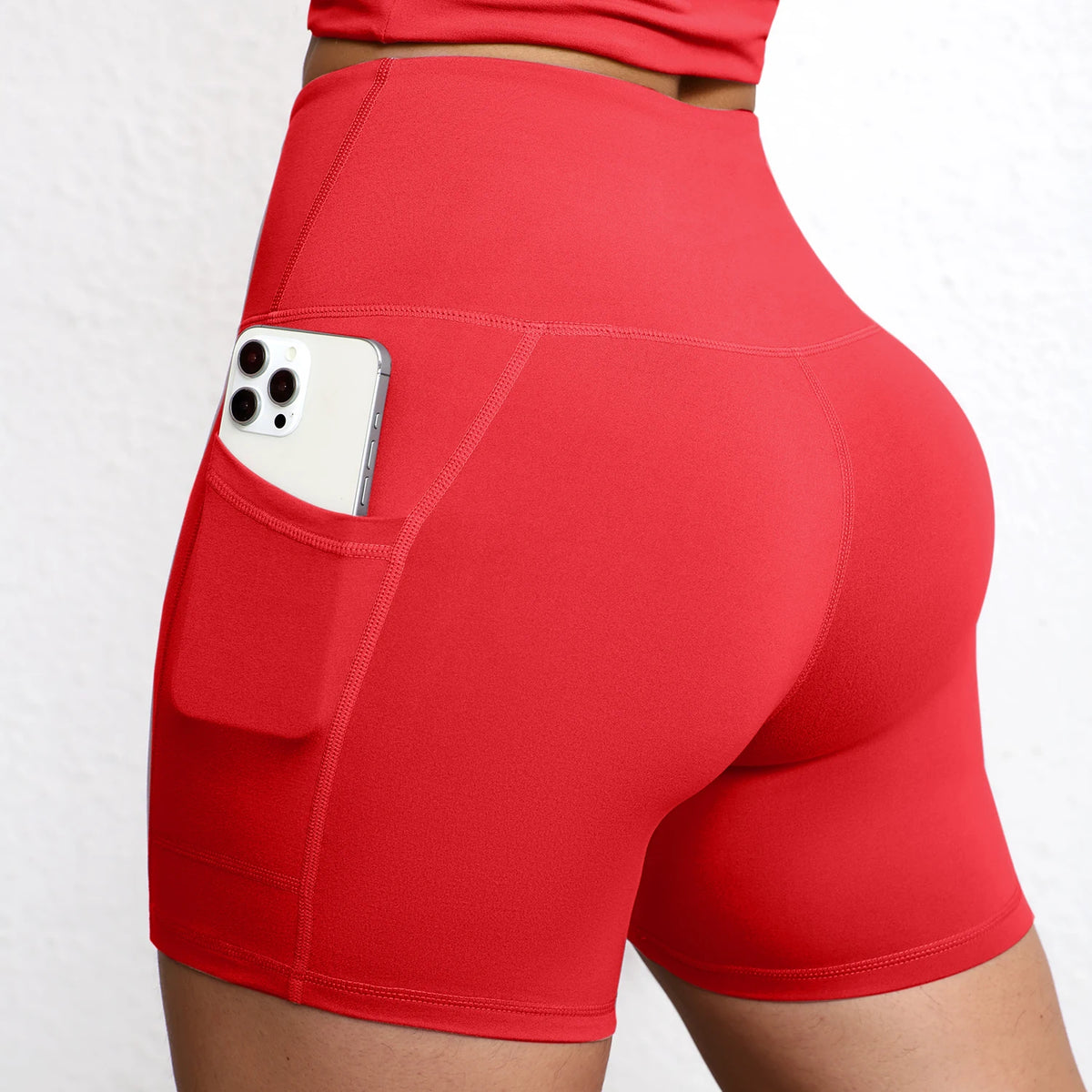 High-waisted seamless yoga shorts in vibrant red, featuring a side pocket with a smartphone, showcasing a sculpted fit.