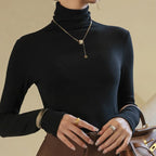 Slim-fit black ribbed mock-neck pullover with long sleeves, worn with layered jewelry and stylishly paired with brown bottoms.