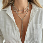 Layered necklace featuring silver beads and a heart pendant, worn over a white button-up shirt, draping elegantly.