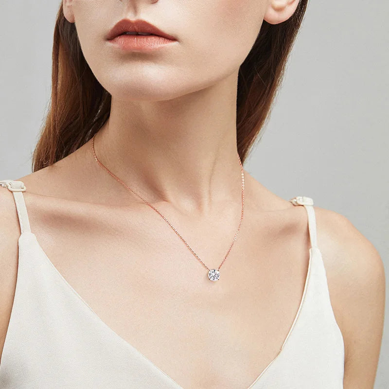Round-cut Moissanite pendant necklace set in rose gold chain, worn against a bare shoulder, showcasing classic elegance.