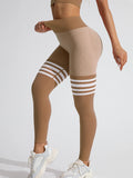 High-rise seamless leggings in tan with white varsity stripes and V-back detailing, worn by a model adjusting the waistband.