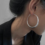 Minimalist chunky hoop earrings in high-gloss silver, worn on the ear of a person with dark hair, styled elegantly.